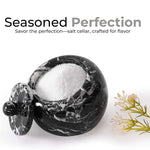 A white marble salt cellar with lid containing pink salt, placed on a white surface with some plant parts in the background.