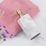 A black marble soap dispenser with a gold pump, placed on a white surface next to a pink towel and a toothbrush.