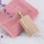 A black marble soap dispenser with a gold pump, placed on a white surface next to a pink towel and a toothbrush.