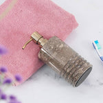 A black marble soap dispenser with a gold pump, placed on a white surface next to a pink towel and a toothbrush.