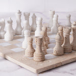 A 15-inch chess set made of travertine stone displayed on a chess board, with multiple pieces including kings, queens, knights, bishops, rooks, and pawns.