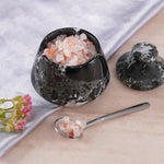 Black marble salt cellar with pink Himalayan salt, spoonful of salt on a wooden surface.