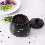 Black marble pepper grinder with peppercorns on a white surface