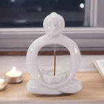 A white marble incense holder in the shape of a sitting Buddha figure with an incense stick placed in the center.