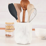 A black marble utensil holder on a kitchen counter, filled with various kitchen utensils.