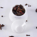 White teapot filled with dried fruits and spices on a white background