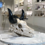 Decorative stone bull skull with black horns on a marble surface in a modern interior setting.
