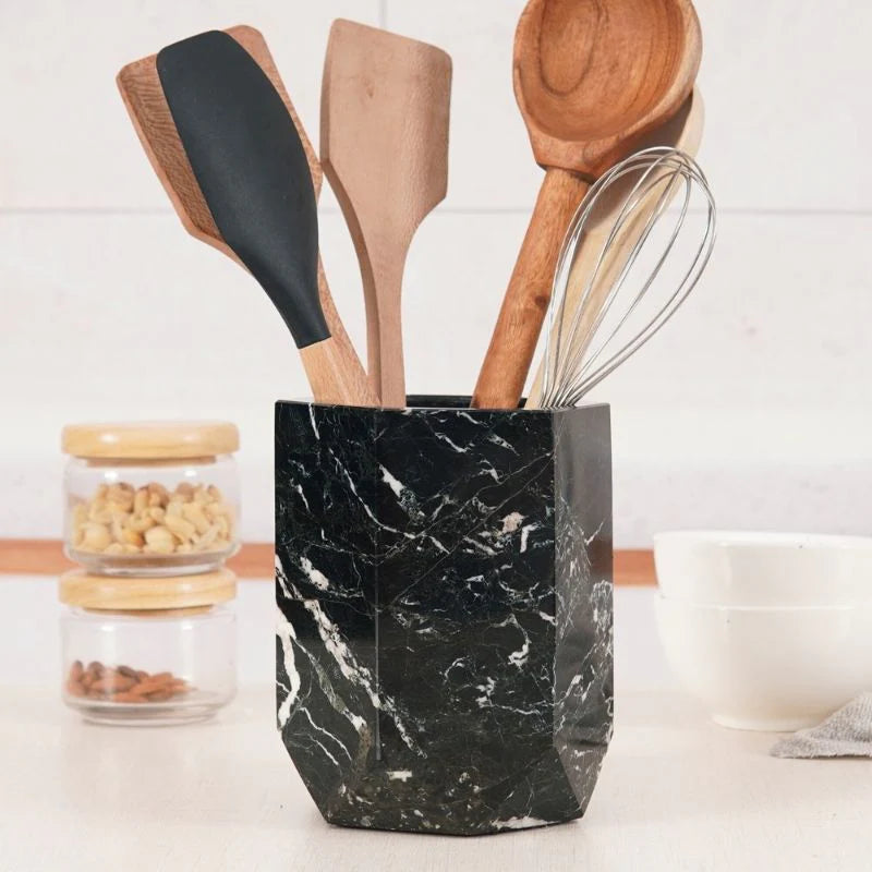 A black marble utensil holder on a kitchen counter, filled with various kitchen utensils.