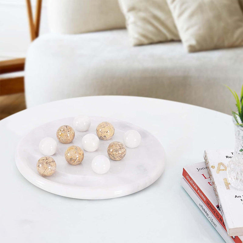 A Tic Tac Toe board with white and coral marble balls on a table, with a couch and a plant in the background.